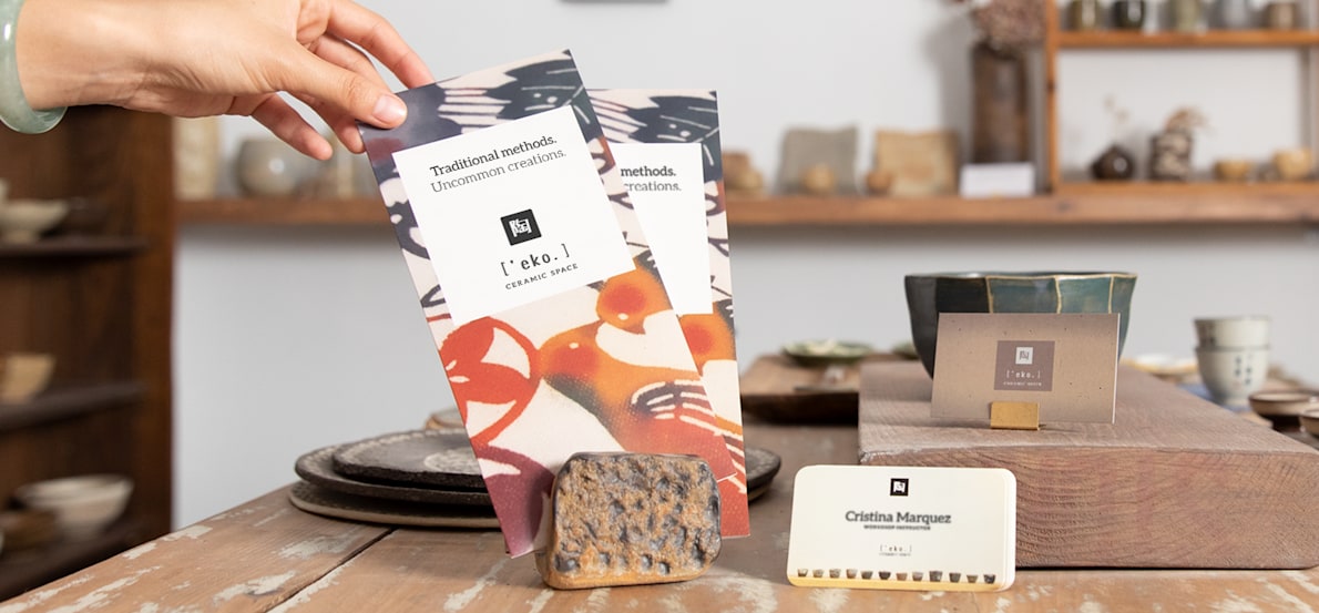 Hand reaching for a vertical business leaflet displayed in a ceramic workshop.  