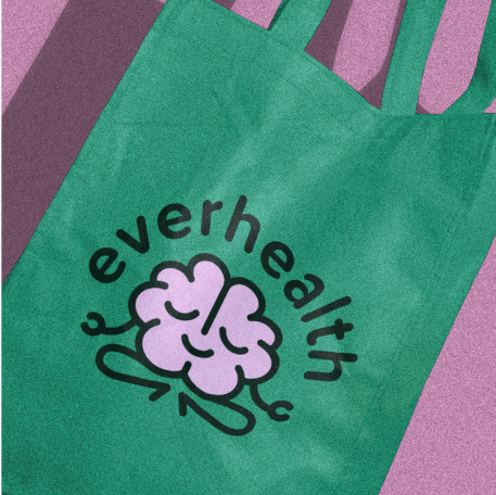 A green tote bag with a smiling purple brain illustration and the text "everhealth" printed on it.
