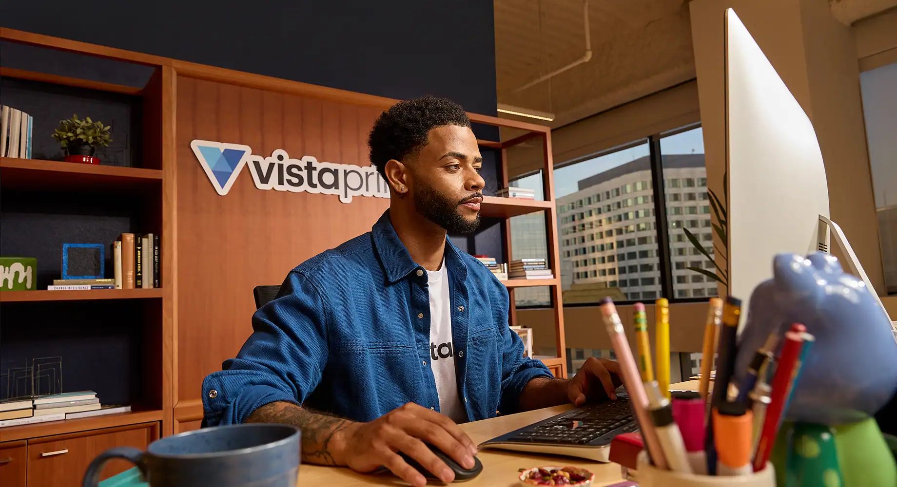 A professional VistaPrint designer working at a desk creating a custom logo on a computer.