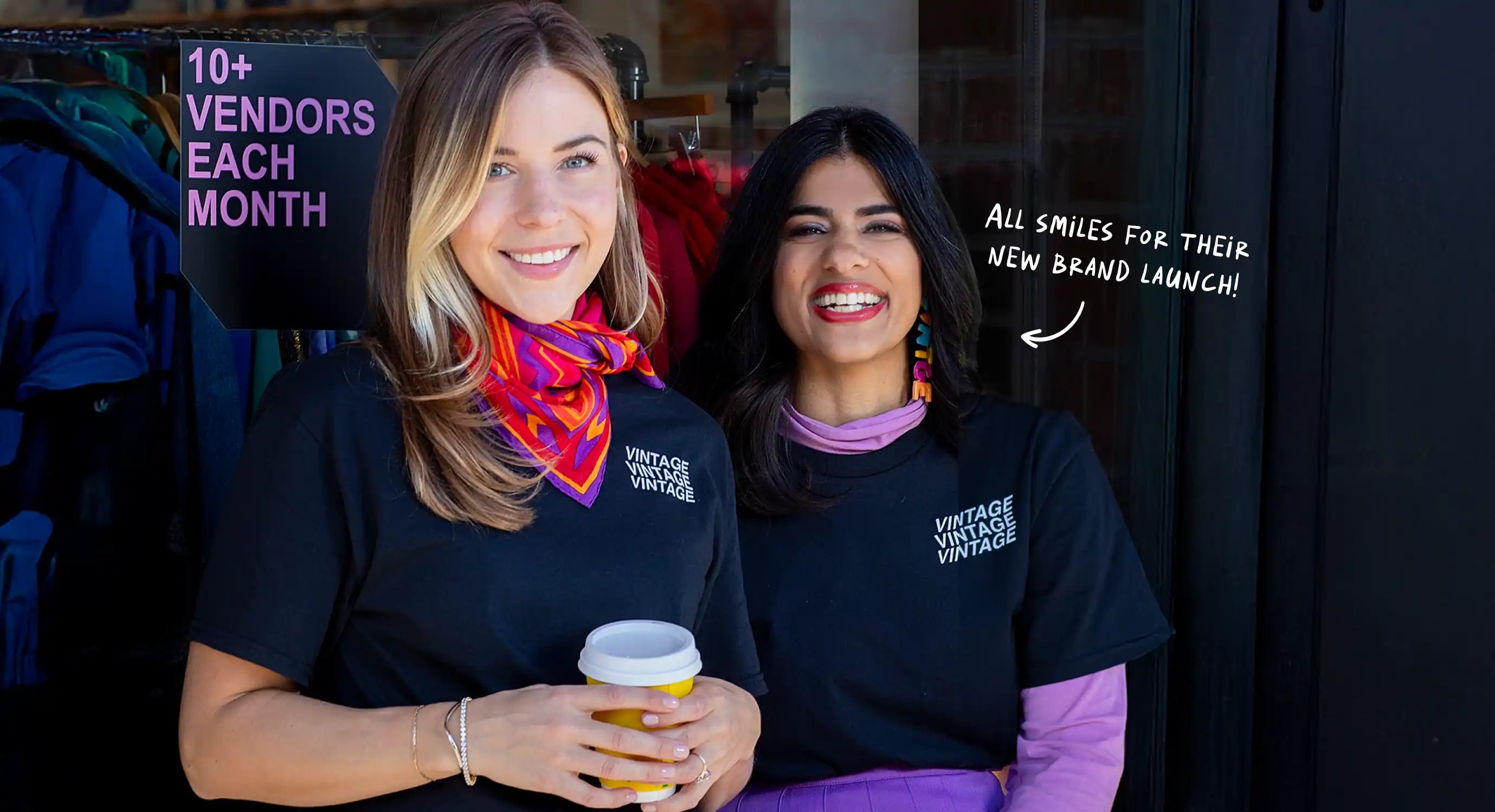 Two female co-owners of a newly launched vintage clothing store stand in front of their shop, dressed in black shirts, smiling happily