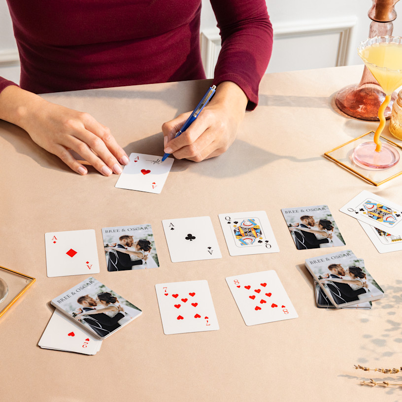 An individual sitting at a table signing playing cards customized with wedding photos.  