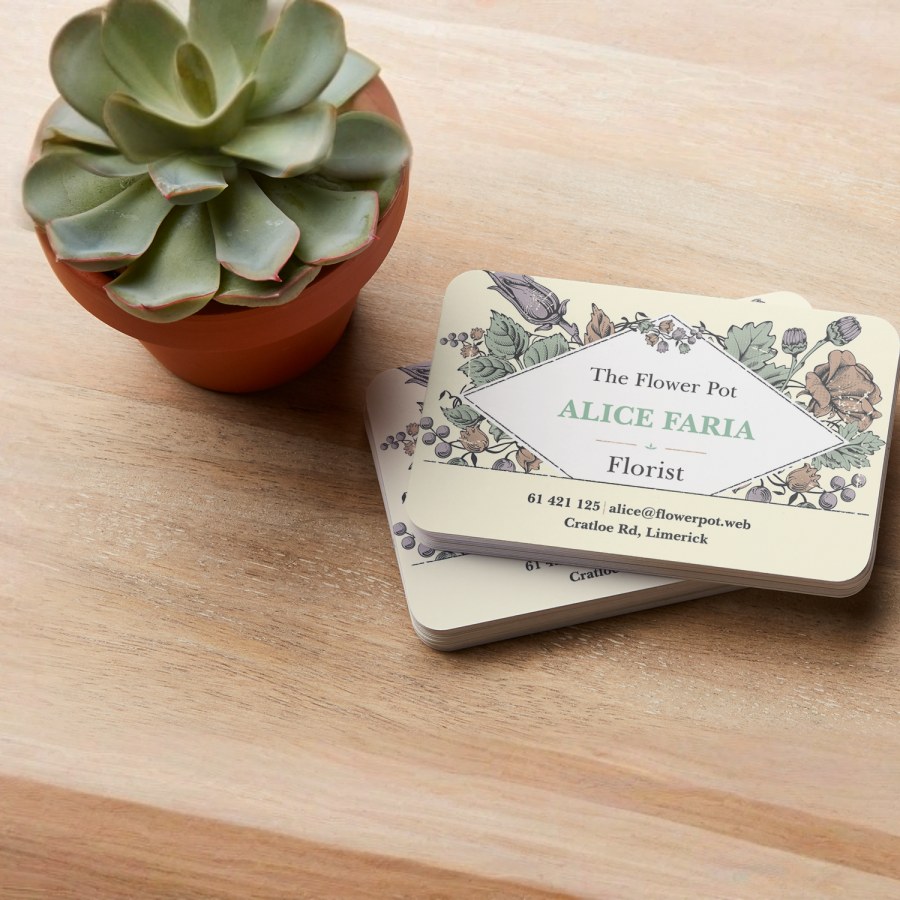 A stack of recycled matte business cards for a florist rests on a wooden countertop next to a succulent.