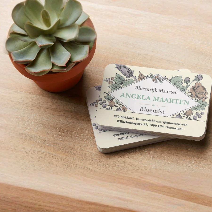 Een stapel gerecycled matte visitekaartjes voor een bloemist ligt naast een vetplant op een houten toonbank.