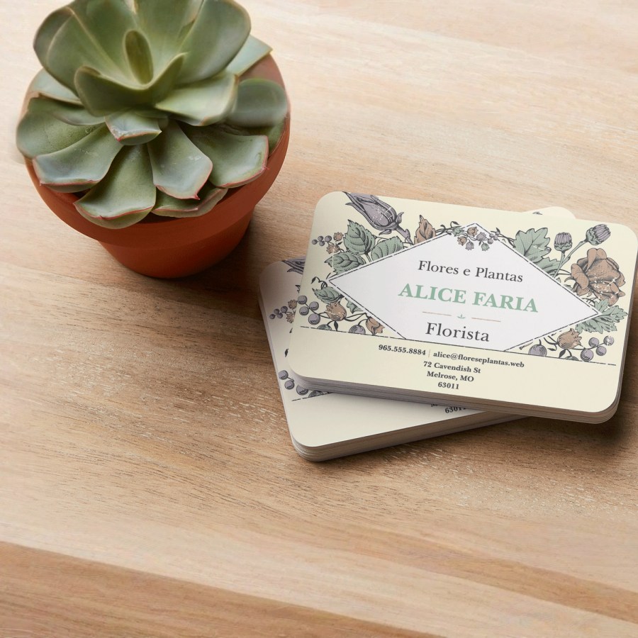 Cartões de visita mate reciclado empilhados para uma florista, dispostos numa bancada de madeira ao lado de uma suculenta.