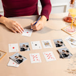 An individual sitting at a table signing playing cards customized with wedding photos.  