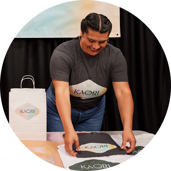 Eine Frau faltet personalisierte T-Shirts mit dem Logo Ihrer Firma „Kaori“ auf einer Messe.