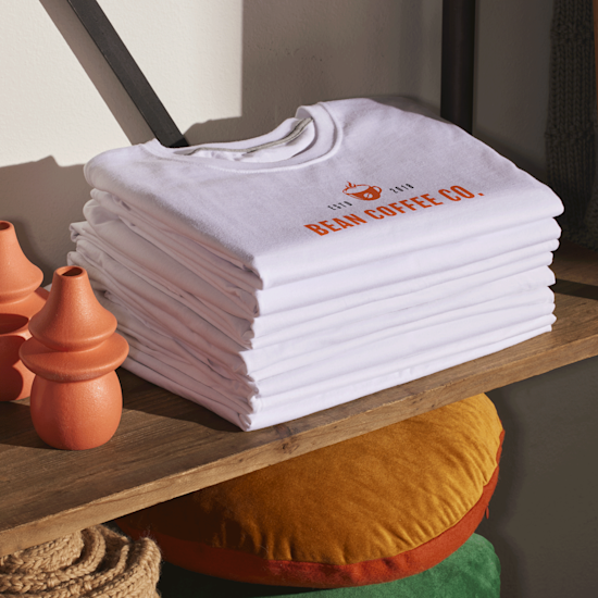 Una pila di t-shirt personalizzate bianche appoggiata su un ripiano di un negozio