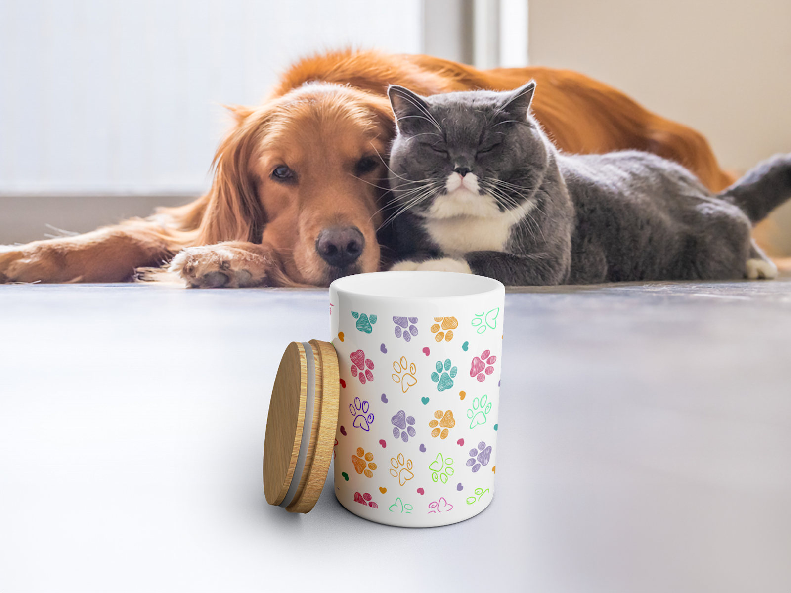 Ein Hund und eine Katze blicken auf eine Leckerlidose aus Keramik mit stilisierten Pfotenabdrücken. 