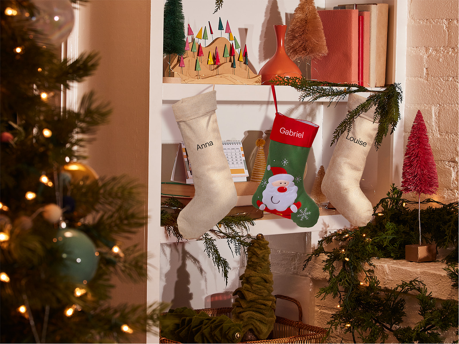 Drei individuelle Nikolausstrümpfe mit Namen, aufgehängt an einem Regalbrett voller Weihnachtsdeko.