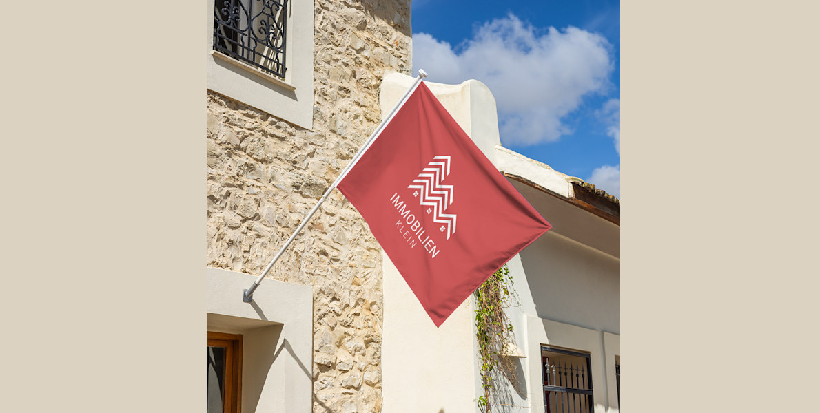 Die Flagge eines Maklerbüros weht über einem Haus.