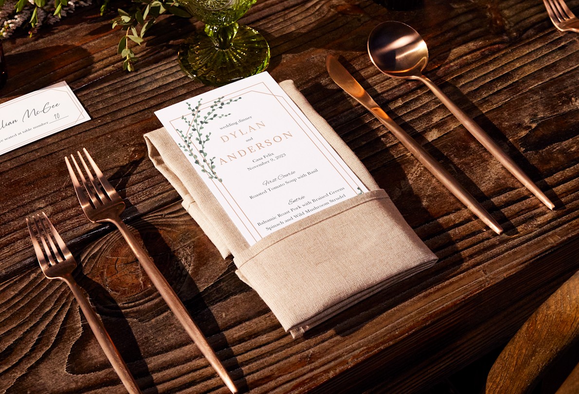 Larger version: A wedding menu with a modern design rests on a beige napkin on a wood table.