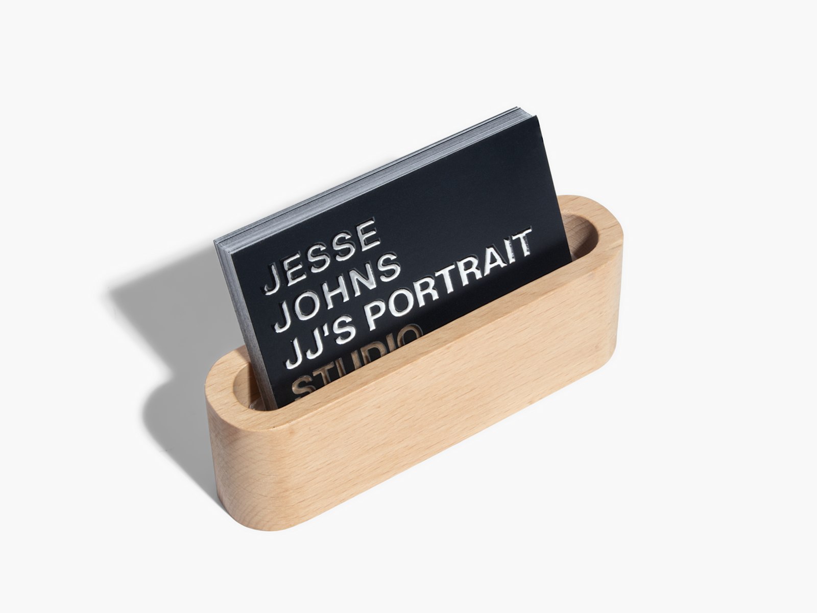 Raised foil business cards promoting a portrait studio, in a wooden business card holder.