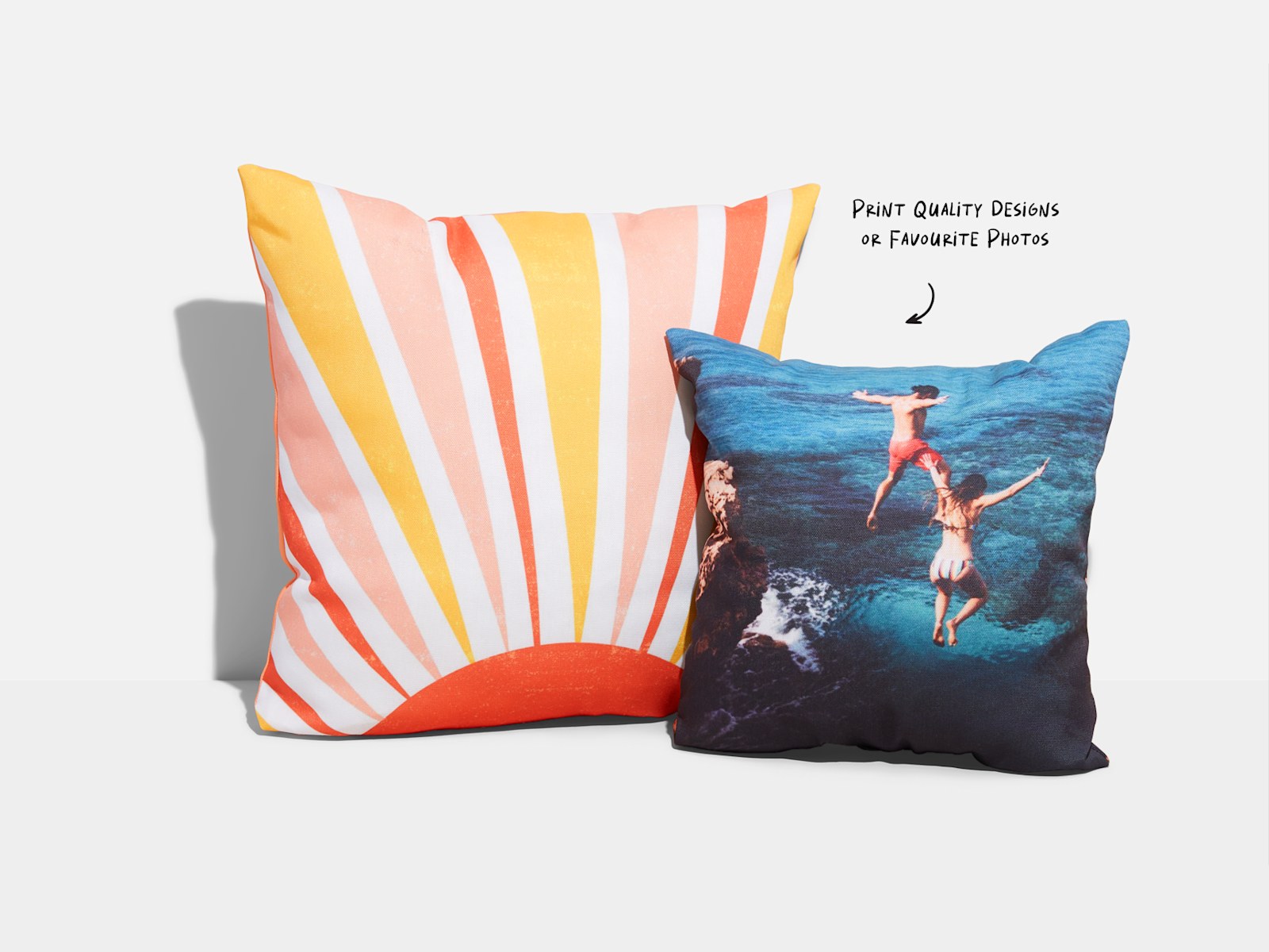 One custom pillow featuring a graphic-based design and the other featuring a photo of two people cliff jumping, with a note that you can print quality designs or favorite photos. 
