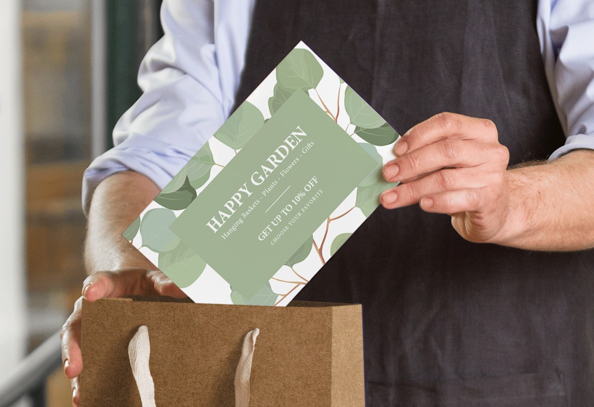 Shop assistant dropping a large green postcard inside a paper shopping bag. 