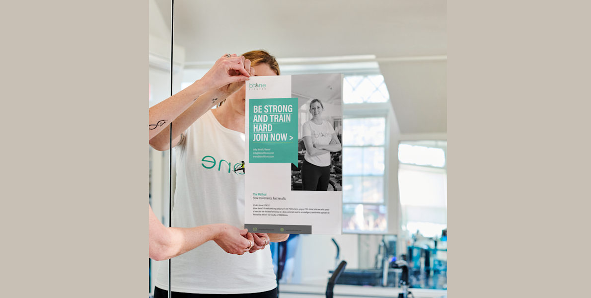 A woman putting up a personalised poster in a fitness studio to promote fitness classes.