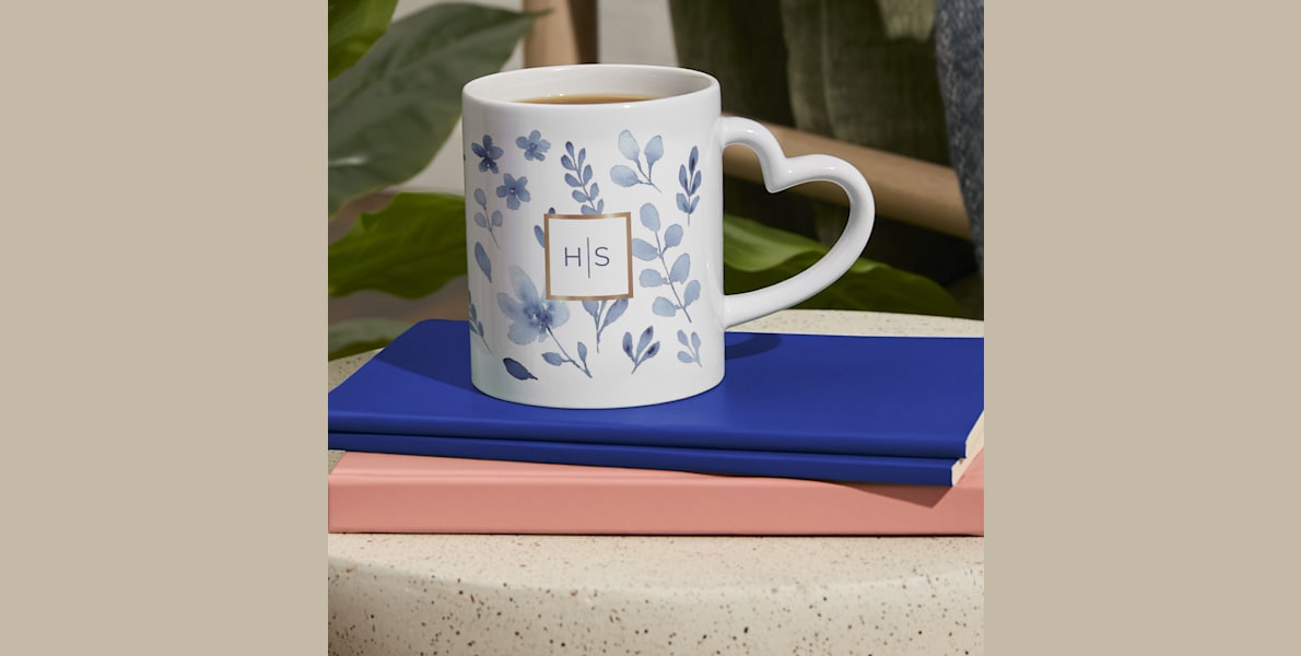 Larger version: A heart-shaped handle mug with a custom monogram resting on a stack of books.  