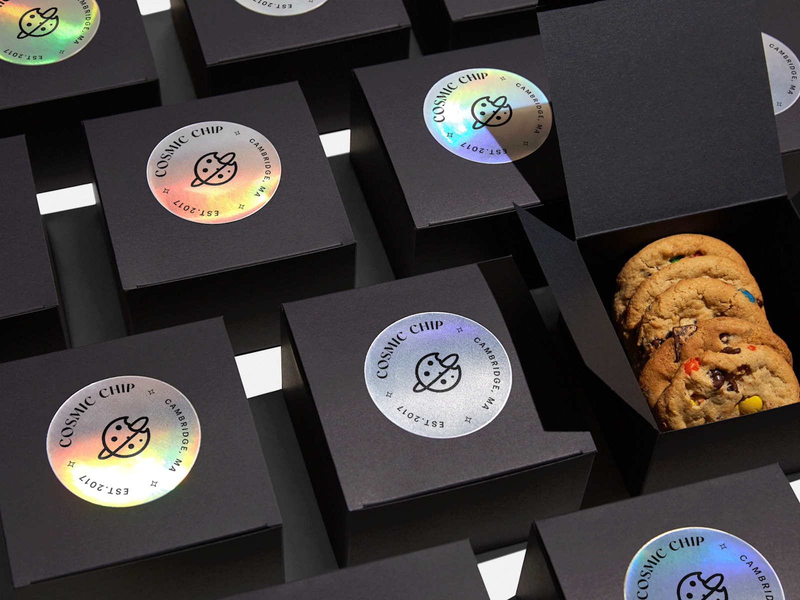 Black boxes neatly lined up in rows with circle holographic paper sticker labels applied to the top of each. One box is opened revealing cookies inside