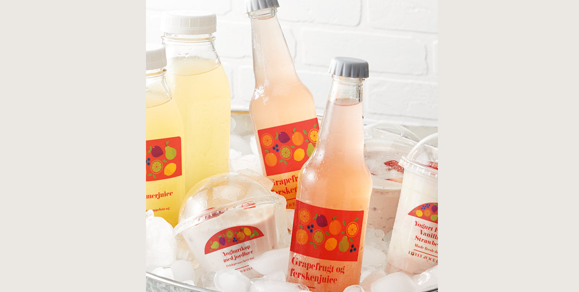 Various bottles of juice and yogurt cups arranged in a bucket of ice. Each bottle and yogurt cup is affixed with a clear plastic label.