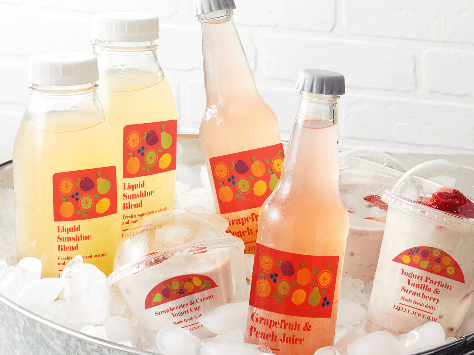 Various bottles of juice and yogurt cups arranged in a bucket of ice. Each bottle and yogurt cup is affixed with a clear plastic label.