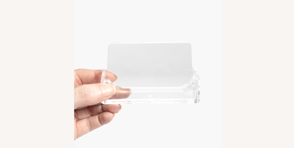 An acrylic business card holder being held in someone’s hand.