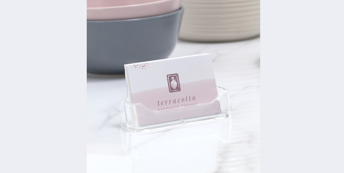 An acrylic business card holder holding business cards for a ceramics studio.