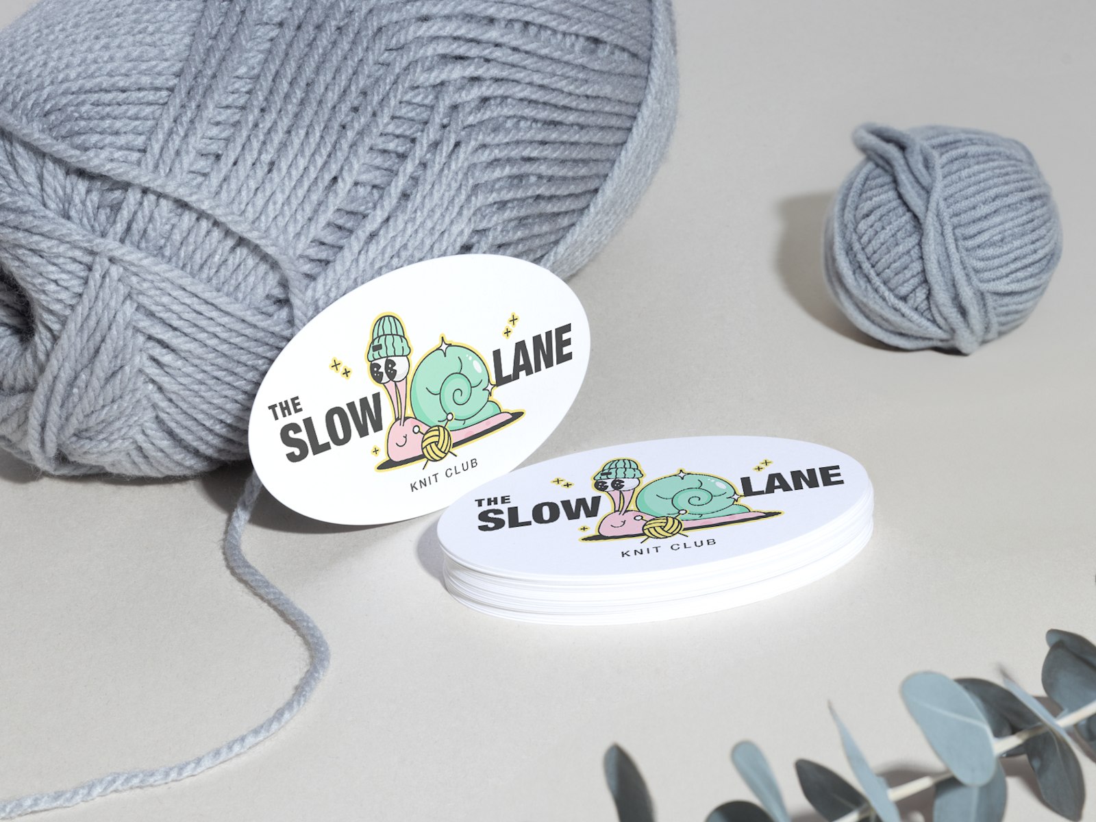 A stack of oval business cards for a knitting club, with yarn and plants in the background.