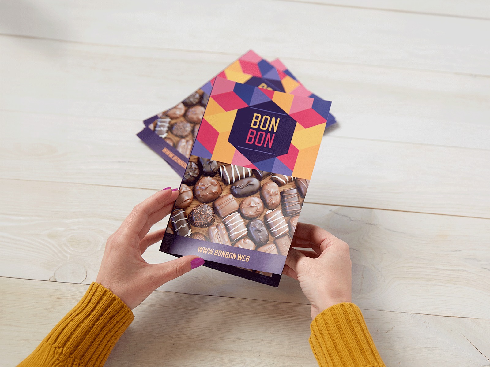 A person holding a bi-fold menu for a chocolate shop, with a stack of bi-fold menus in the background.