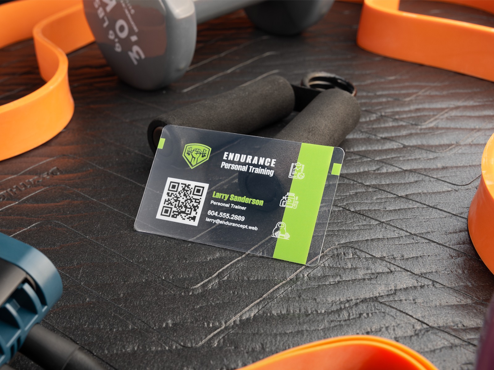 A clear plastic business card for a personal trainer, with exercise equipment in the background.