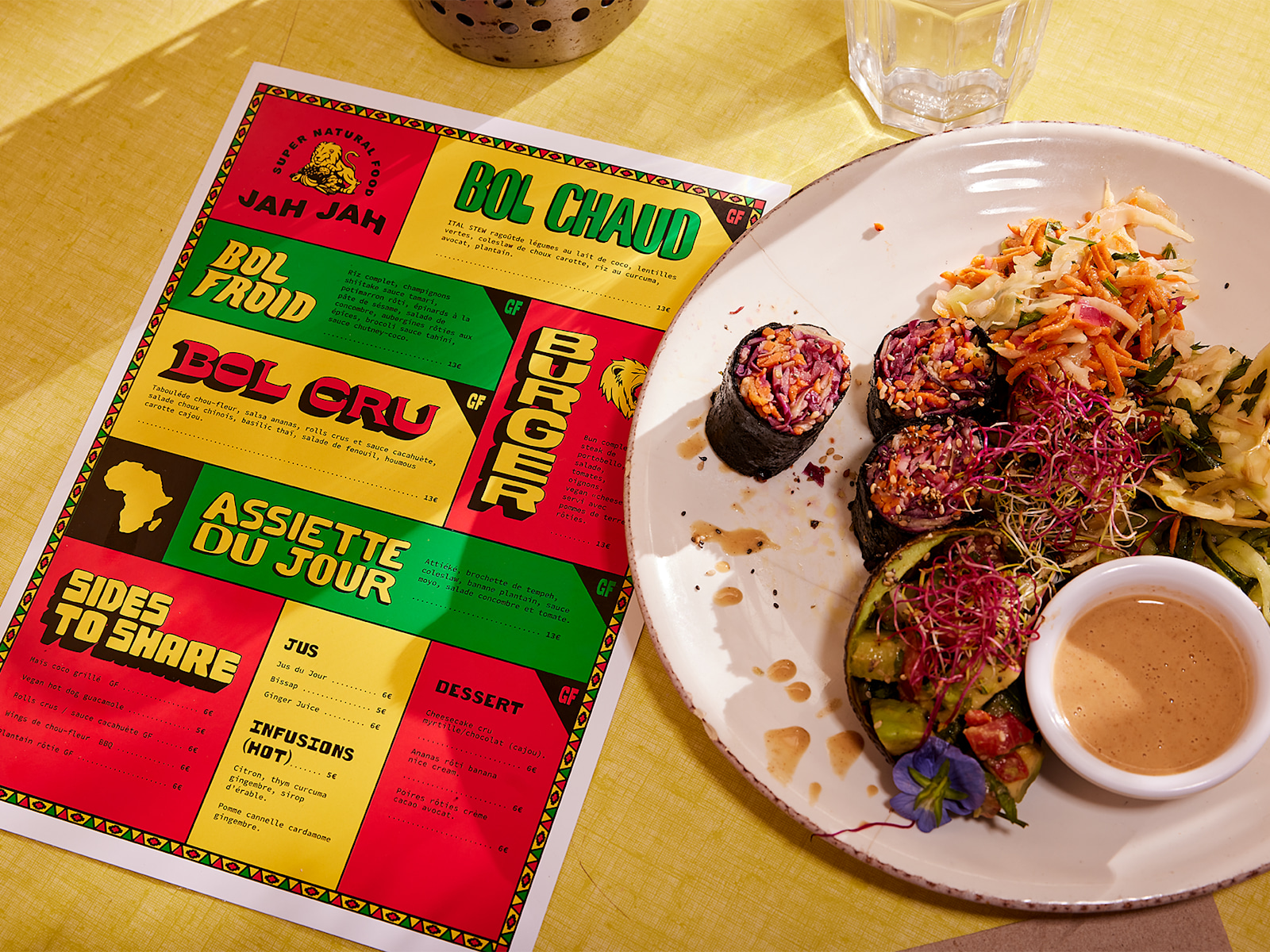 A colorful flat menu at a place setting in a restaurant, next to a dish of food. 