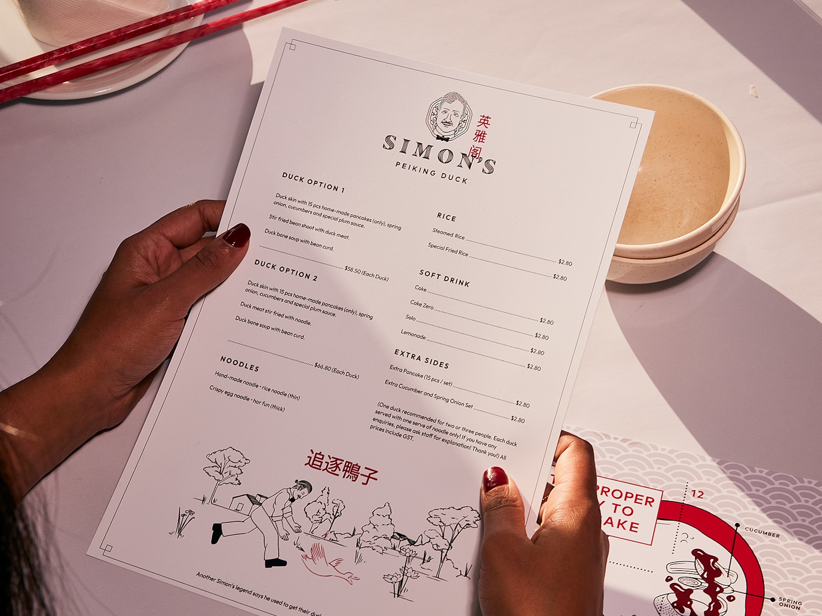 A diner holding a menu for a Chinese restaurant, just above their place setting.