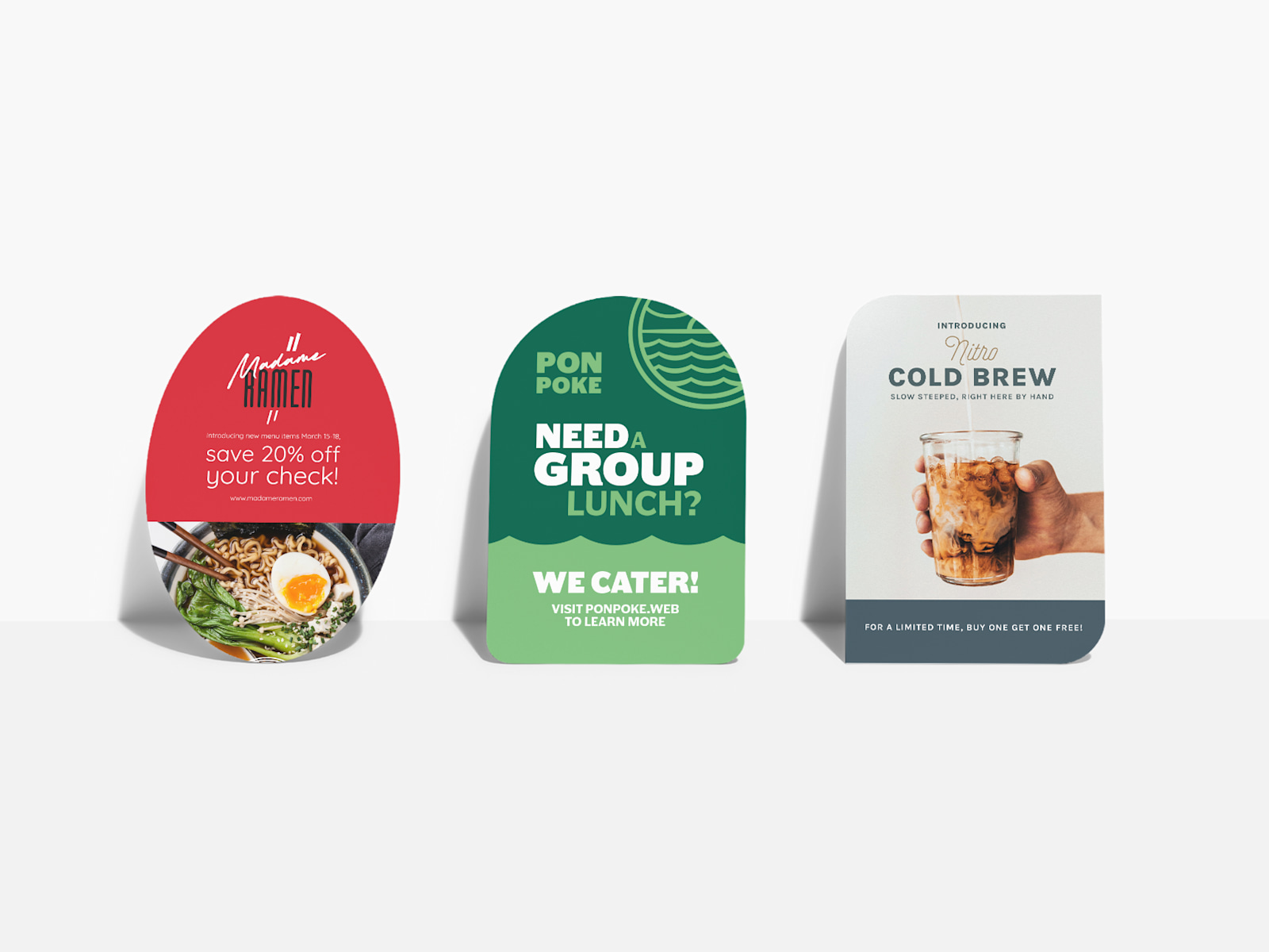 Oval, half-circle and leaf-shaped postcards, all propped up against a wall and advertising different restaurants.