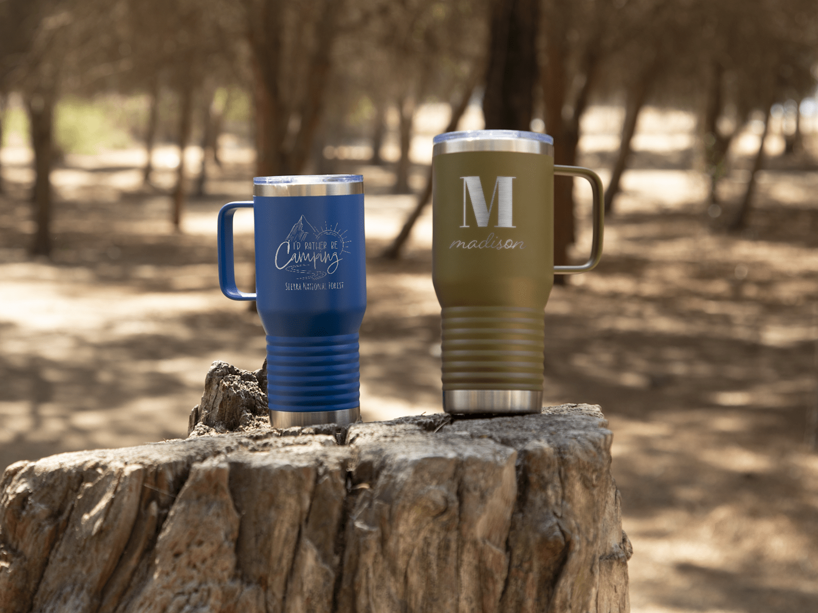 Larger version: Two custom travel mugs resting perched on a rock in the woods. 