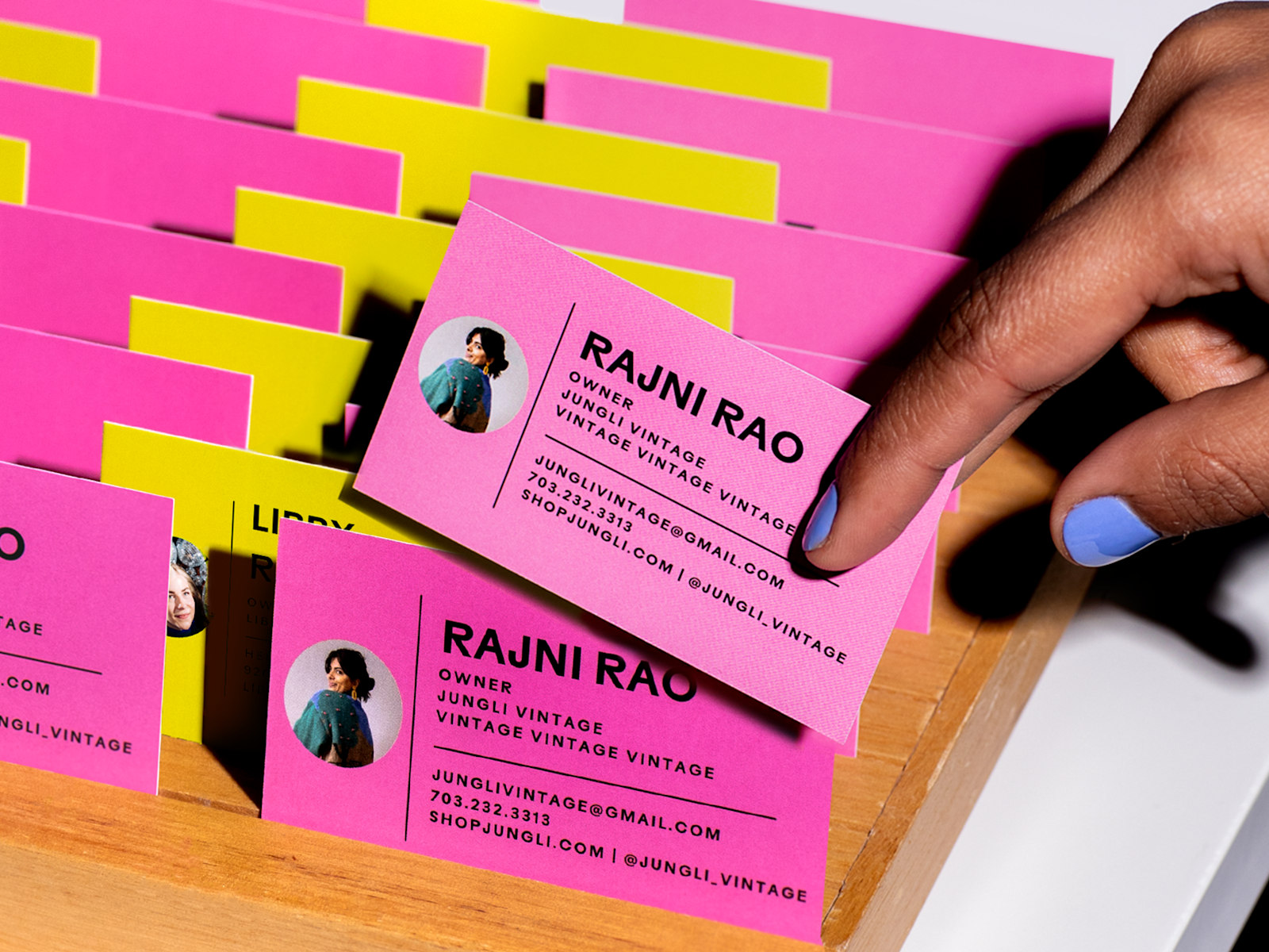 Larger version: Pink and yellow business cards for a vintage shop in a wooden holder, with a hand pulling one out.