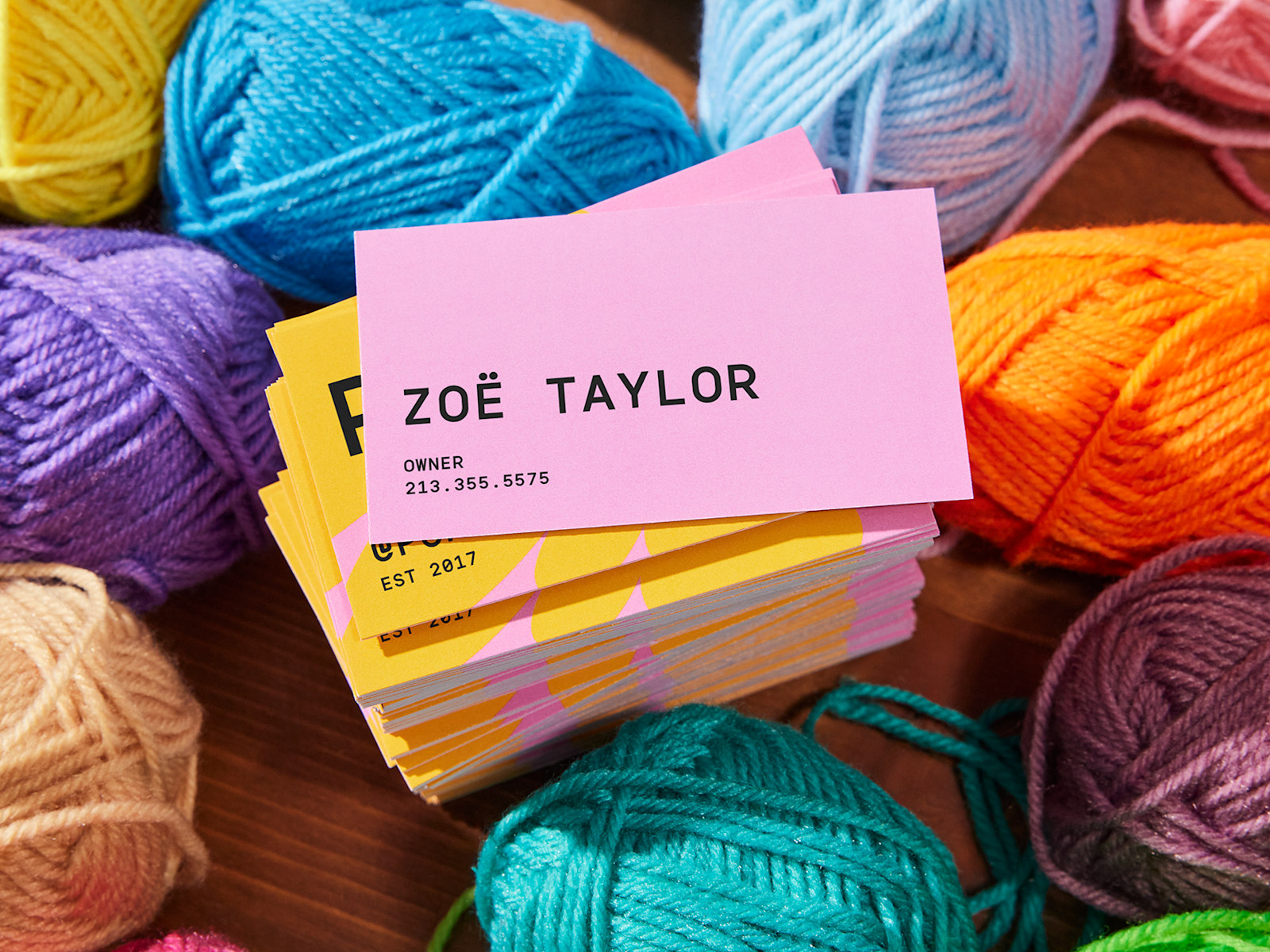 A stack of business cards placed on colorful yarn balls, with the top card showing the backside design.