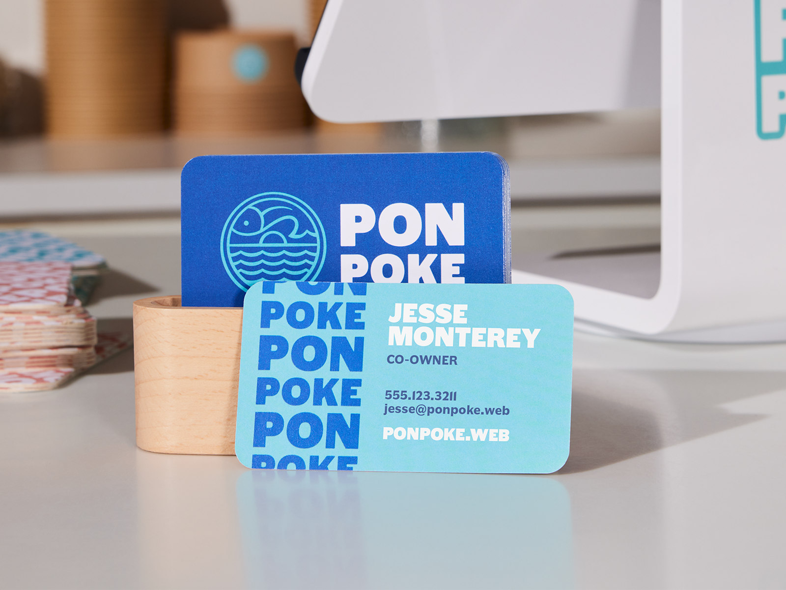 A set of blue and white rounded corner business cards for a poke restaurant, placed on a checkout counter.
