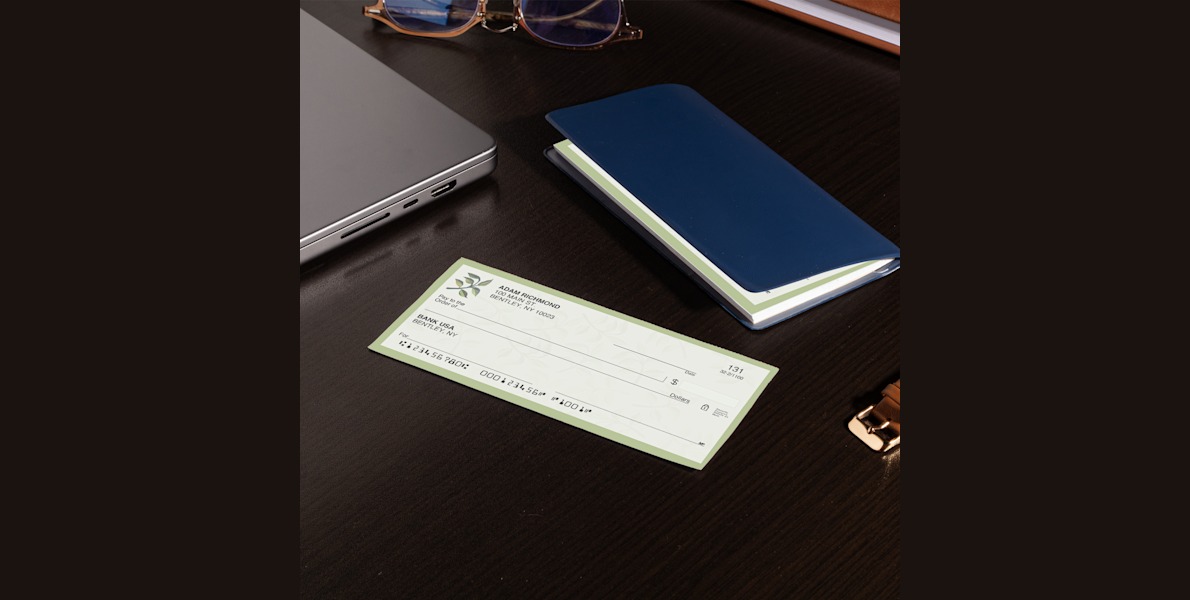 Larger version: A wallet check on a desk next to a checkbook, laptop and other office supplies.