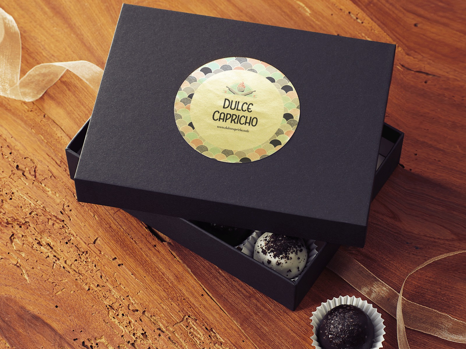 Una caja negra colocada sobre una mesa de madera sin la tapa que revela los dulces adentro. La tapa tiene una etiqueta redonda dorada pegada.