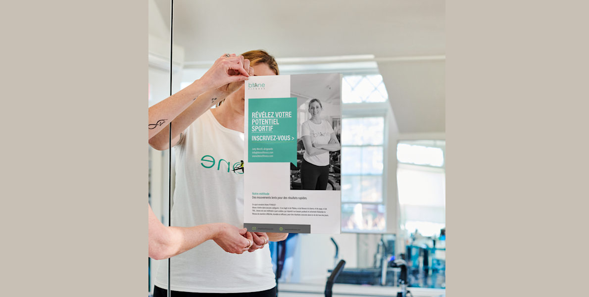 Femme accrochant une affiche personnalisée dans un centre de remise en forme pour faire la promotion de cours de sport.