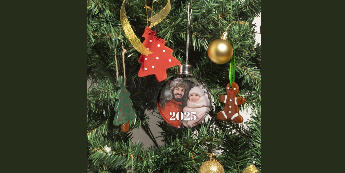 Aan een kerstboom hangt een kerstbal met foto, gepersonaliseerd met een foto van een vader en zijn dochter in winterkleding. 