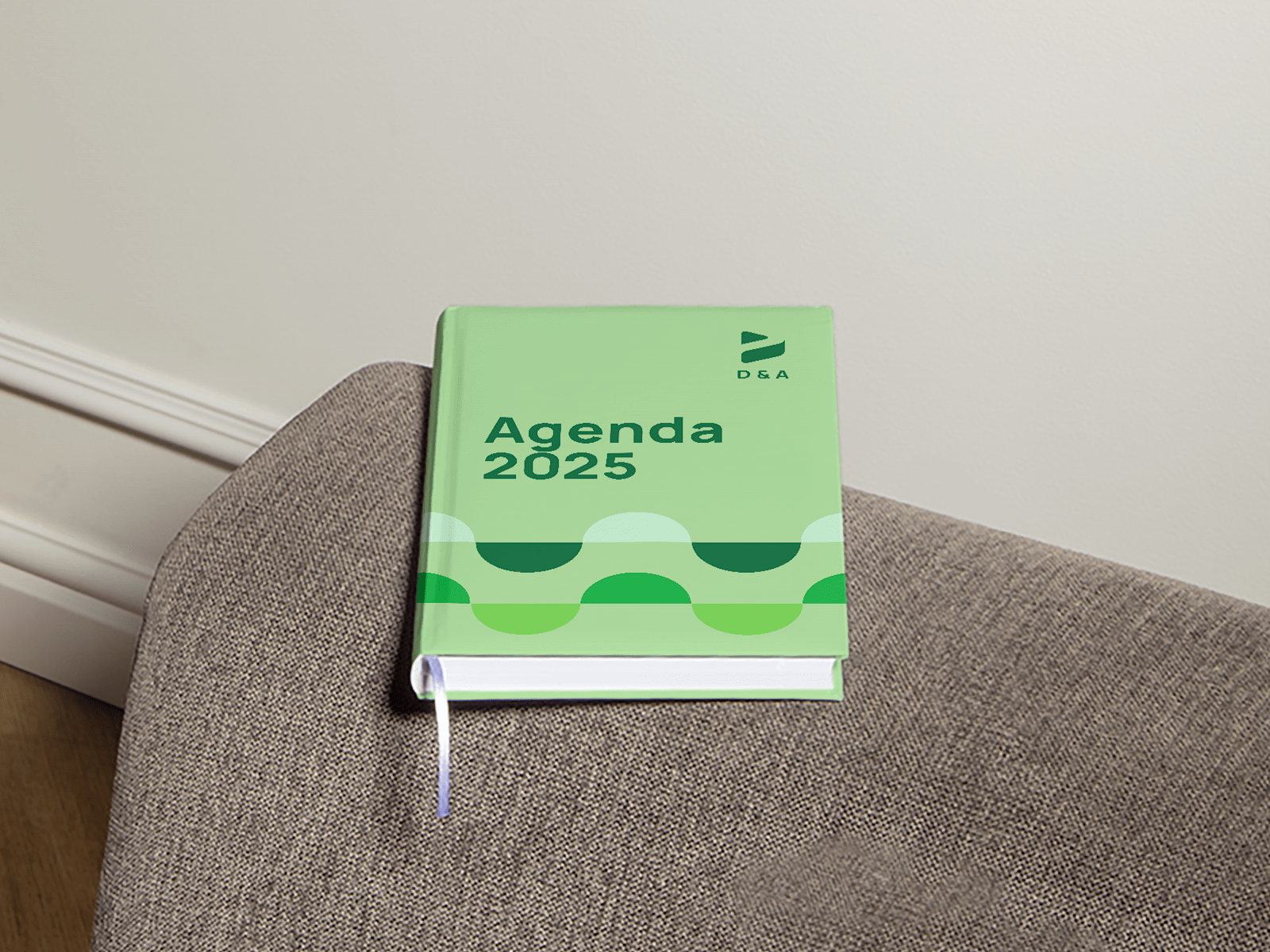 Uma agenda com capa dura em cima do braço de um sofá, a promover uma empresa de design.