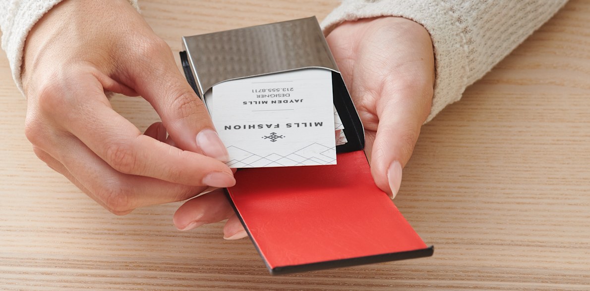 A woman is removing a card from a black leather vertical business card holder.