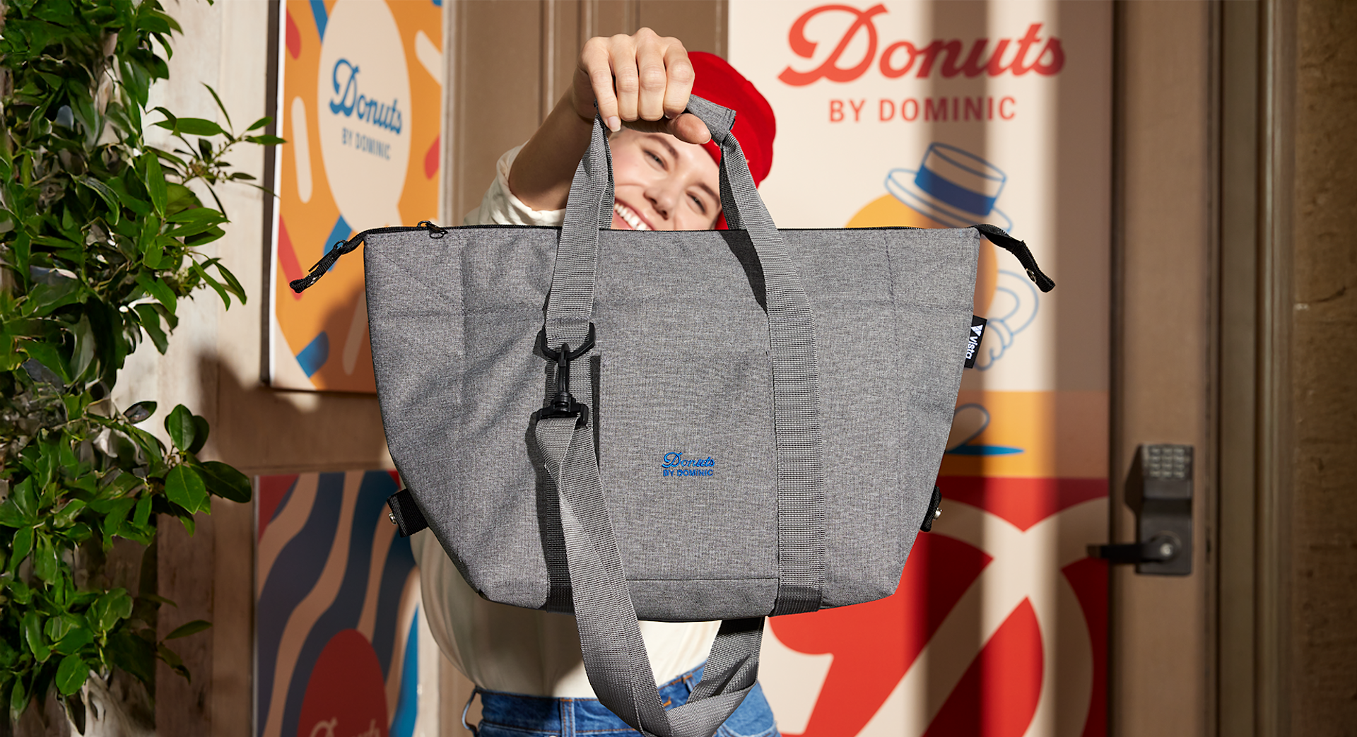 Smiling person holding a custom zippered tote bag in front of a donuts business stand.
