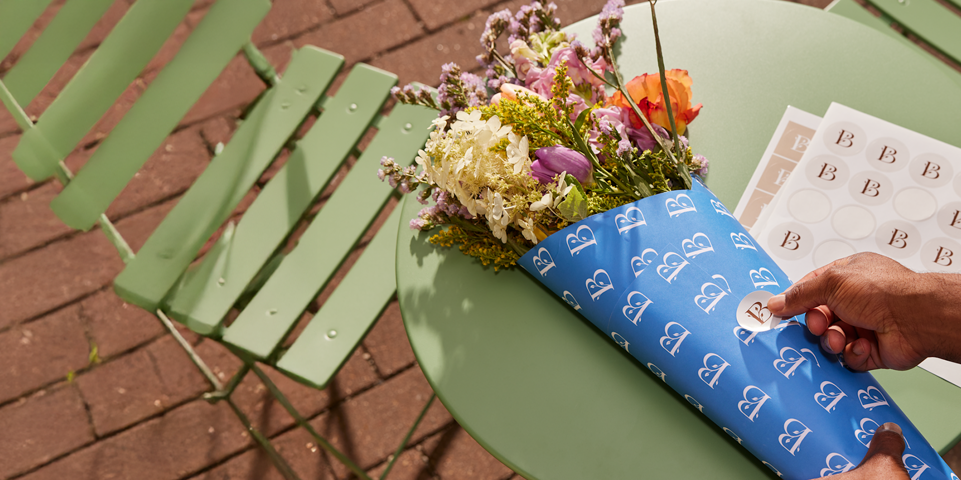 A person taking a sticker from a sheet and using it to seal the wrapping for a bouquet of flowers.