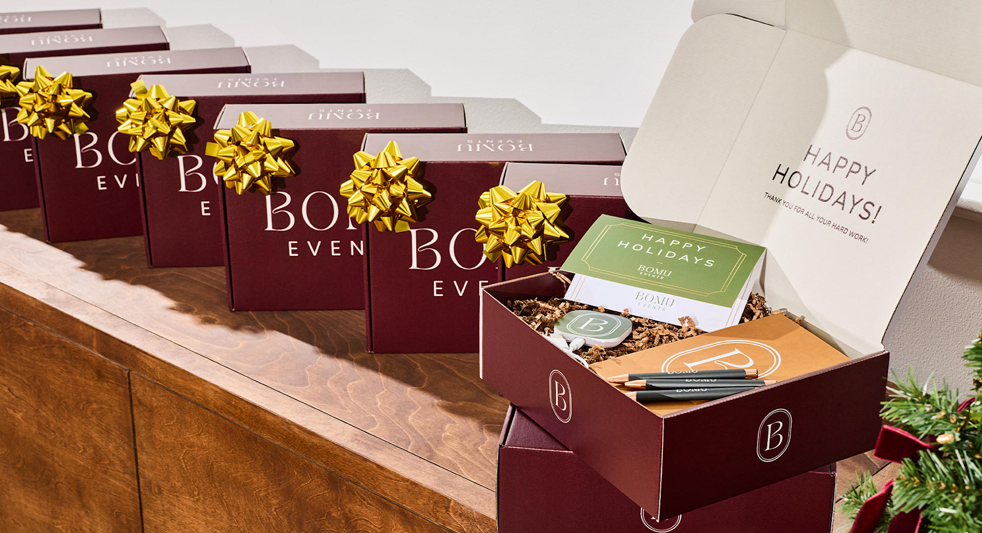 Display of Bomi holiday gift boxes with gold bows and a happy holidays card, with an open brown box showing packaged treats inside. 