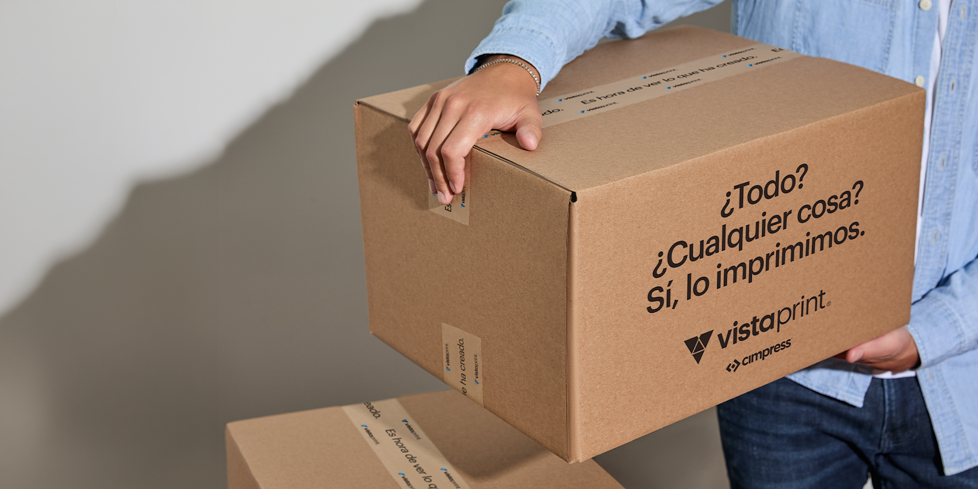 Persona sosteniendo una caja de cartón para envíos de VistaPrint, que representa una entrega rápida.