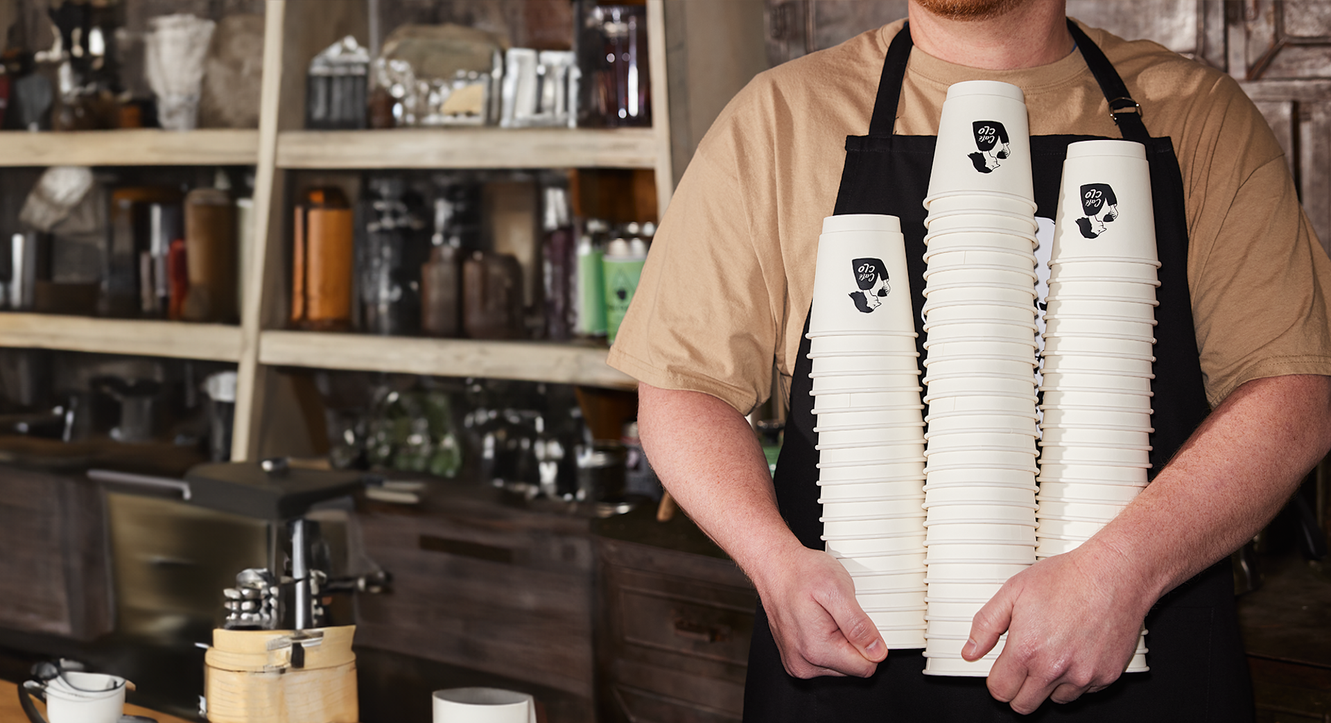 A person holding stacks of paper cups promoting a cafe. 