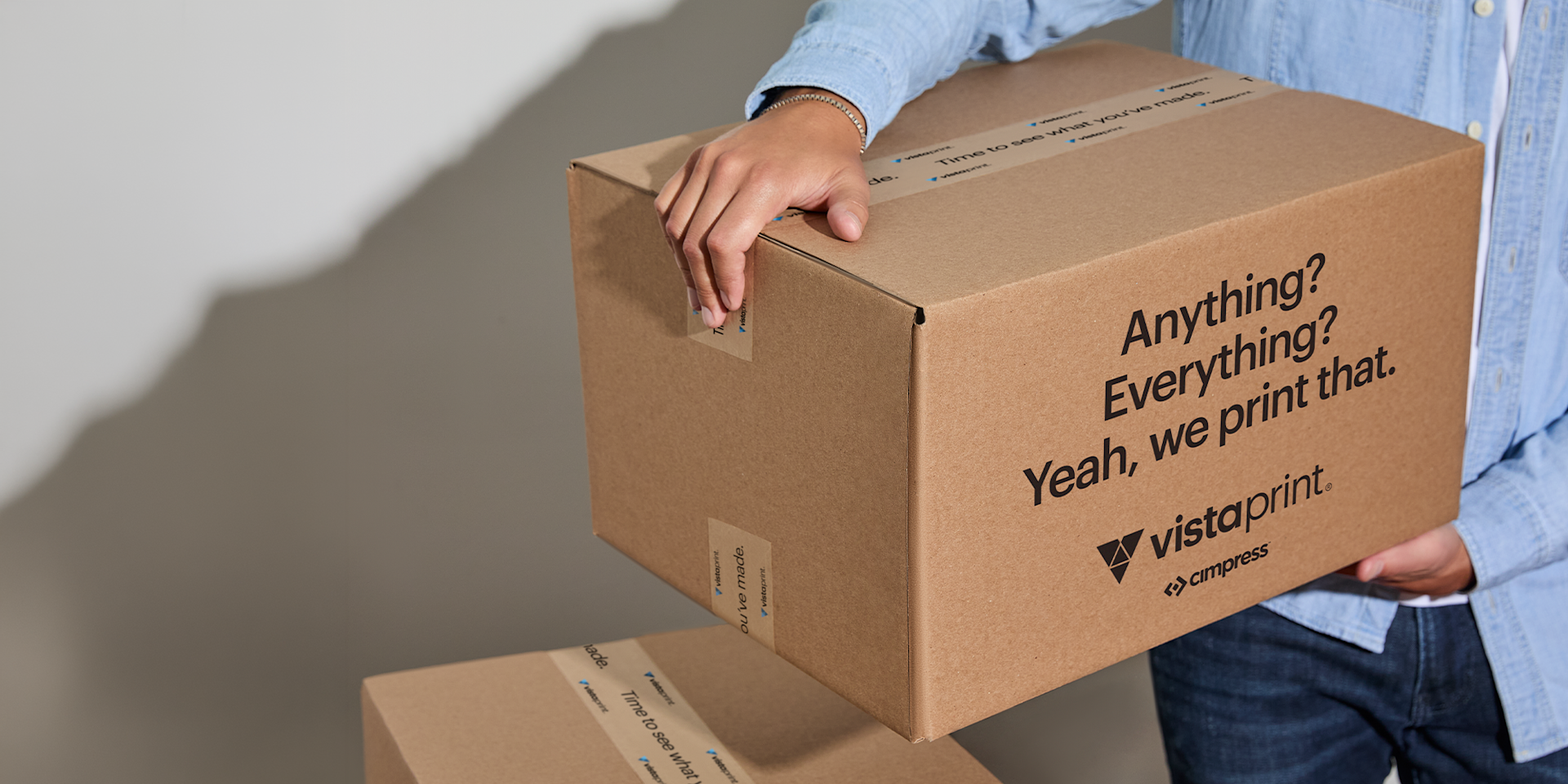 Person holding a Vistaprint branded cardboard shipping box picturing fast turnaround.