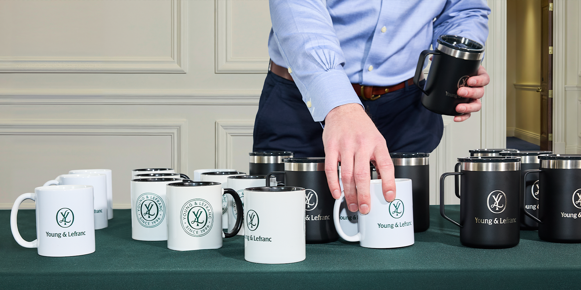 A person arranging custom branded tumblers and mugs promoting a law office business.