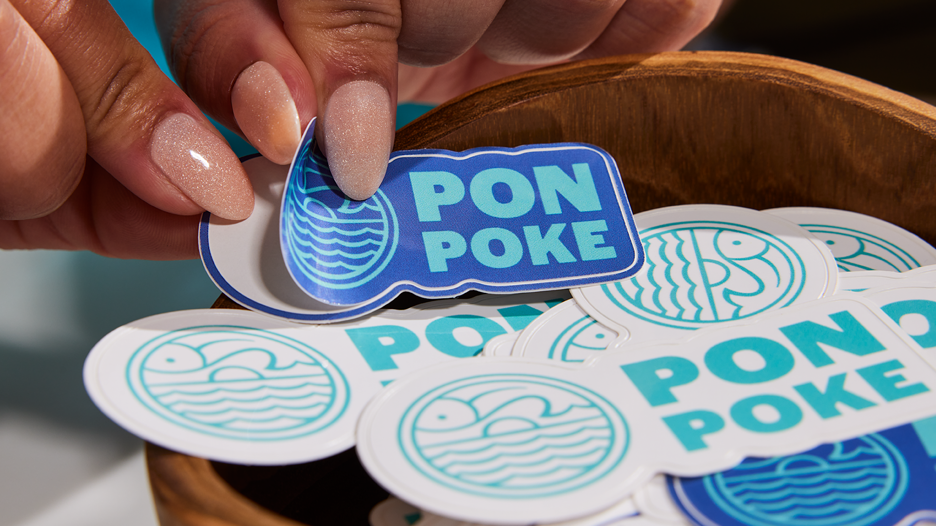 A customer’s hand reaching into a bowl and peeling off a poke bowl restaurant sticker. 