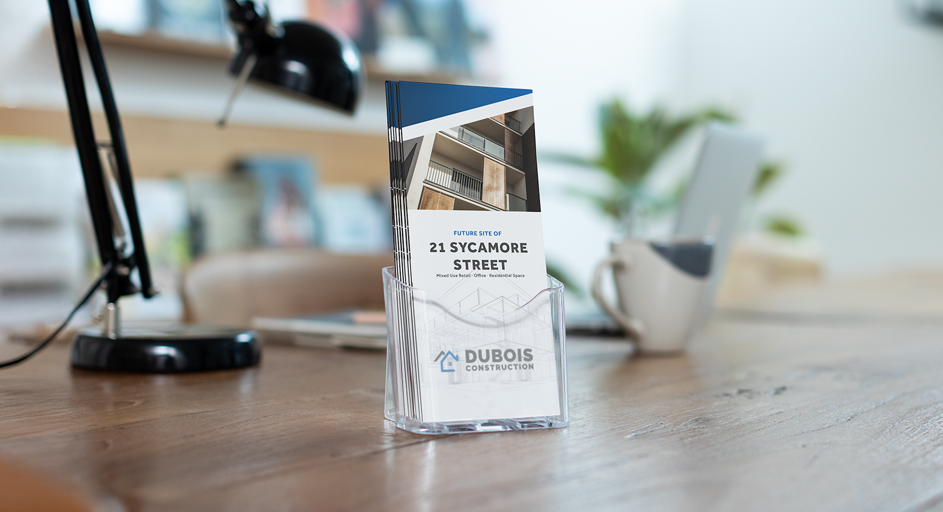 A brochure for a construction company displayed in a clear holder on a wooden desk, with office items in the background.